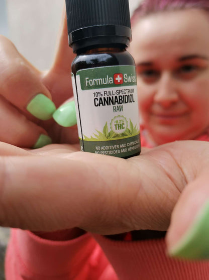 Hand holding a 10% full-spectrum bottle of Formula Swiss RAW CBD oil in hemp seed oil